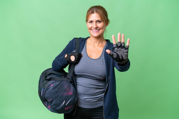 Donna sportiva di mezza età con borsa sportiva su sfondo isolato contando cinque con le dita