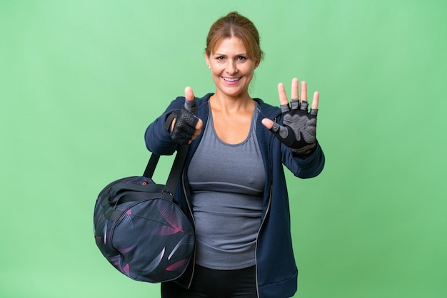 Donna sportiva di mezza età con borsa sportiva su sfondo isolato contando sei con le dita