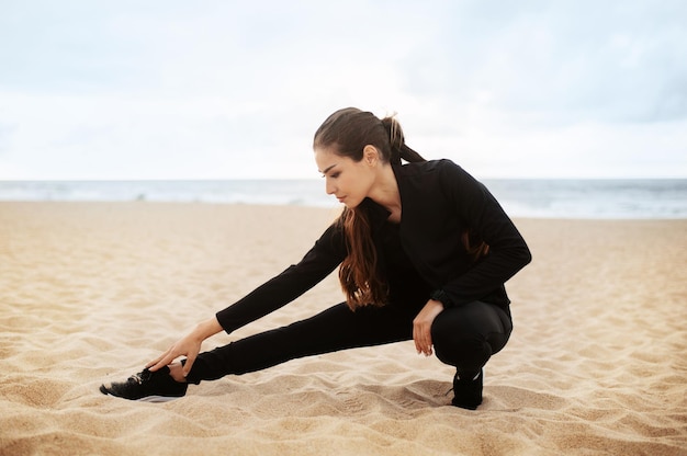 Donna sportiva in allenamento attivo sulla spiaggia che allunga i muscoli delle gambe mentre si prepara per l'esercizio