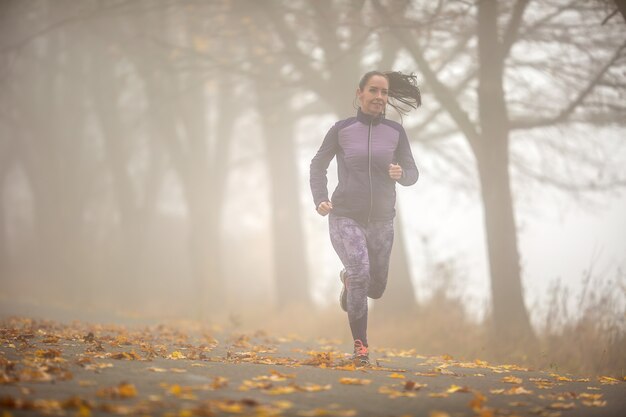 Donna sportiva in esecuzione nella natura nebbiosa autunnale.