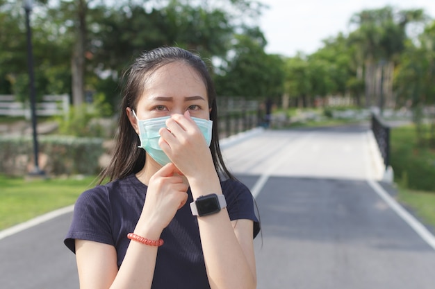 Donna sportiva in maschera protettiva medica rilassante nel parco.