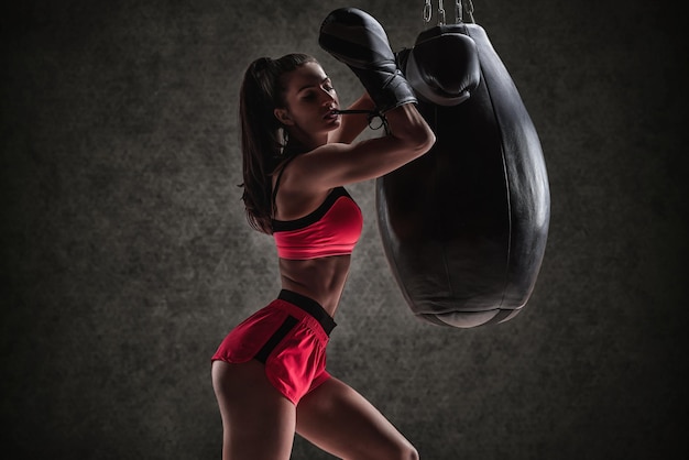 Donna sportiva in pantaloncini rossi e un top slega i guanti con i denti vicino alla borsa Concetto di boxe e arti marziali miste