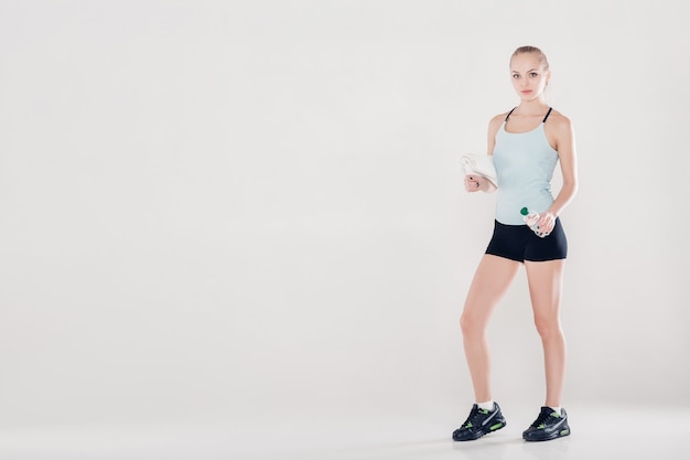 donna sportiva sana in abiti da fitness con asciugamano da palestra e bottiglia d'acqua. luce soffusa