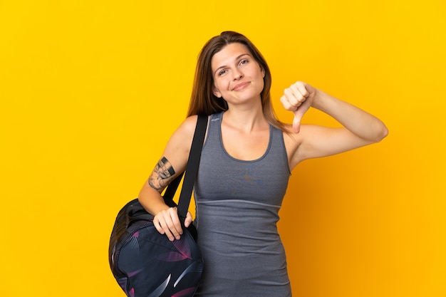 Donna sportiva slovacca con borsa sportiva isolata su sfondo giallo che mostra il pollice verso il basso con espressione negativa