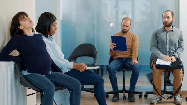 Donna stanca che aspetta un bambino e aspetta in coda con persone nervose per iniziare l'appuntamento per il colloquio di lavoro. Candidata incinta che si sente stressata nell'atrio dell'ufficio alla domanda di lavoro.