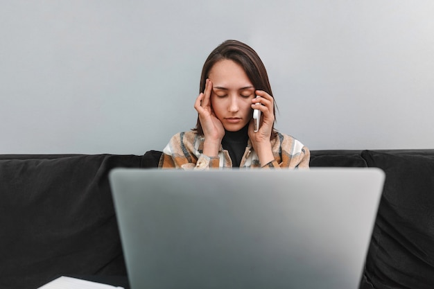 Donna stanca con mal di testa che parla al telefono cellulare e lavora al laptop