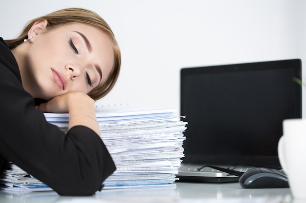 Donna stanca di affari che dormiva su un mucchio di carte al suo posto di lavoro. Superlavoro, lavoro straordinario e stress sul concetto di lavoro.