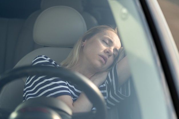 Donna stanca di guidare il sonno sul sedile anteriore femminile che viaggia in auto durante un viaggio su strada che riposa sonnecchiando dentro