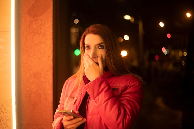 Donna stordita con la mano in bocca che guarda l'obbiettivo in città di notte