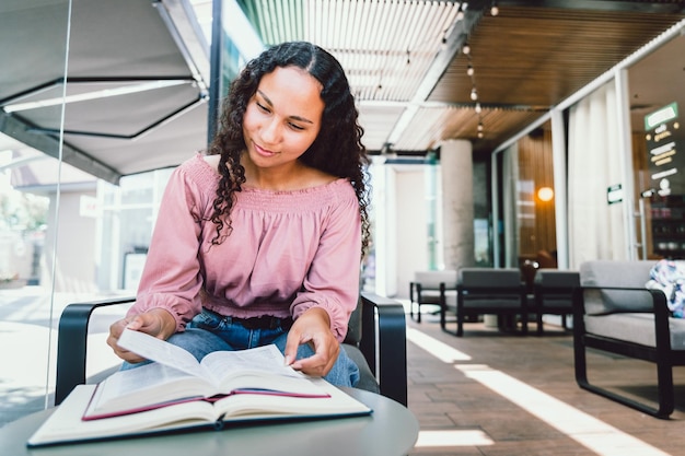 Donna studentessa universitaria latina seduta e che studia per un esame fuori da un caffè. Leggendo libri