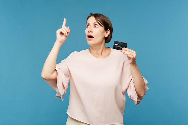 Donna stupita con carta di credito nera sulla parete blu
