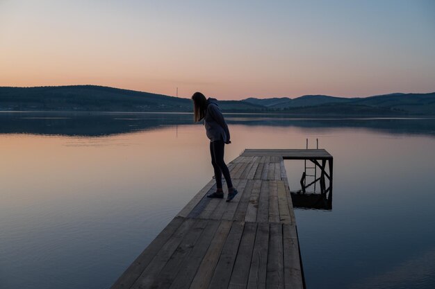 Donna sul molo al lago ritratto di primo piano del tramonto estivo