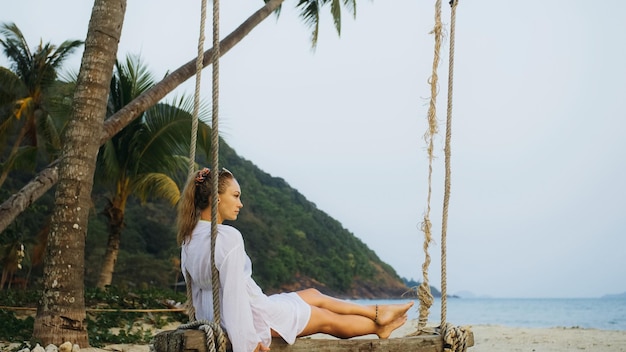 Donna sull'altalena sulla spiaggia tropicale La ragazza in camicia bianca it