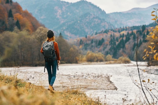 Donna sulla riva del fiume in montagna nella foresta autunnale in vista posteriore della natura