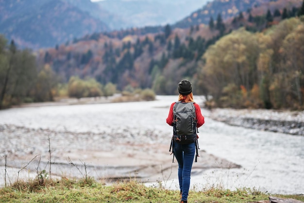 Donna sulla riva del fiume nella foresta e sulle montagne sullo sfondo viaggio turistico del paesaggio