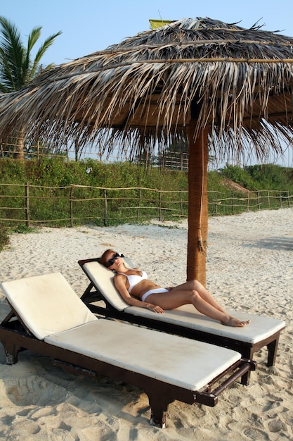 Donna sulla spiaggia sotto l'ombrellone di palma
