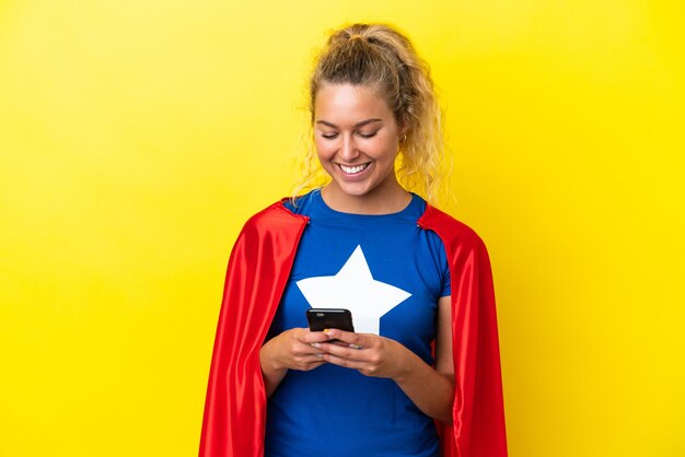 Donna Super Hero isolata su sfondo giallo che invia un messaggio o un'e-mail con il cellulare