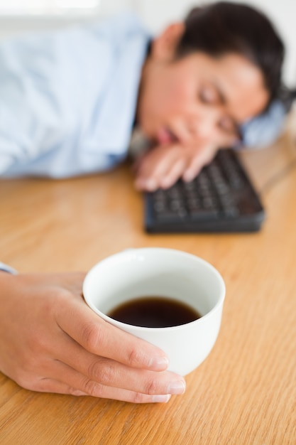 Donna sveglia che dorme su una tastiera mentre si tiene una tazza di caffè