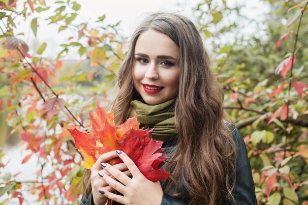 Donna sveglia che sorride e che tiene il concetto di autunno della foglia di caduta