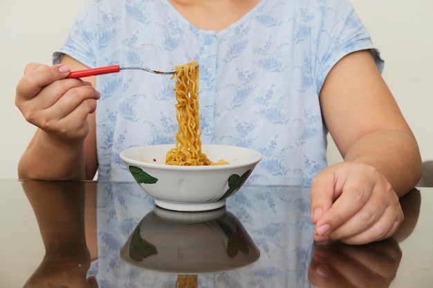 Donna tagliata che mangia noodle fritti piccanti sul tavolo da pranzo
