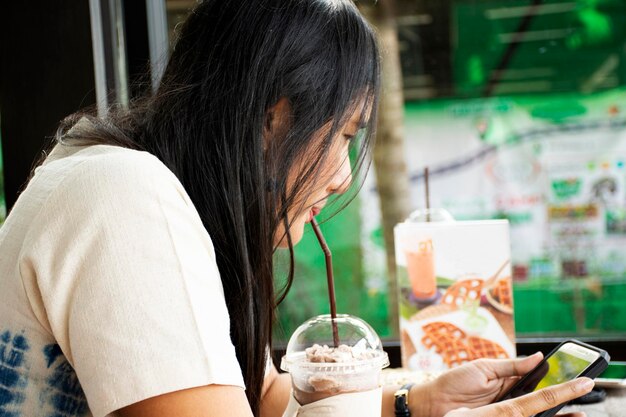 Donna tailandese seduta rilassata giocando smartphone e bevendo cioccolato frappe nella caffetteria il 13 novembre 2018 a Saraburi Thailandia