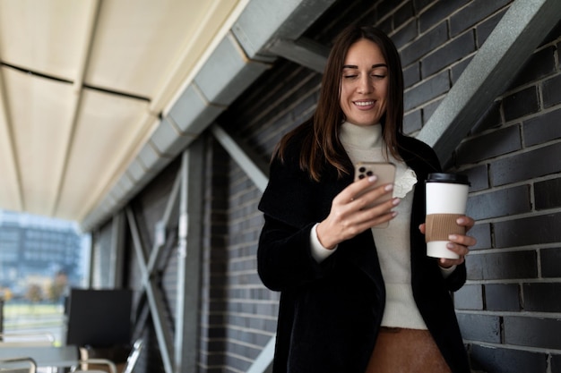 Donna testa bruna alla moda con il telefono cellulare e una tazza di caffè in mano
