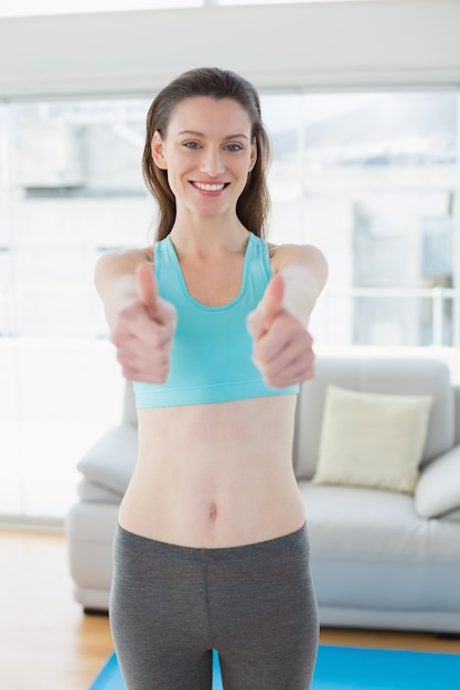 Donna tonificata che gesturing i pollici su nello studio di forma fisica