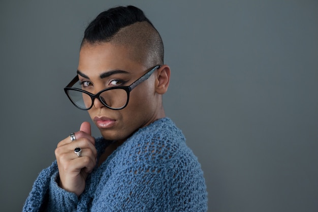 donna transgender che indossa occhiali da vista contro il muro grigio