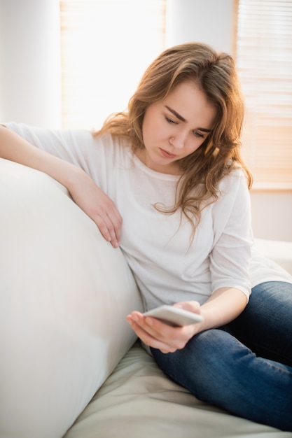 Donna triste che guarda il suo telefono nel salotto