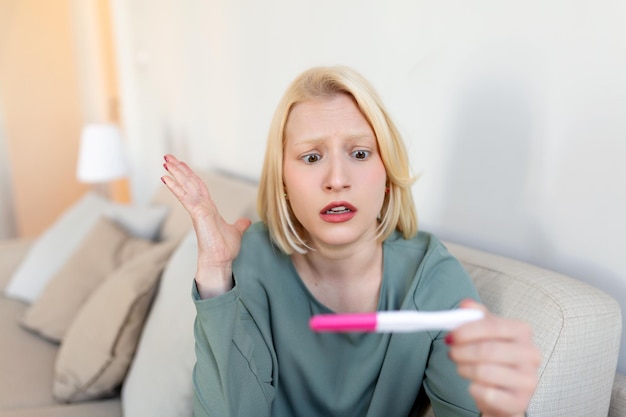 Donna triste e preoccupata che controlla il suo recente test di gravidanza seduto sul divano a casa Concetto di maternità e problemi familiari gravidanza indesiderata