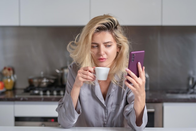 Donna triste in chat sul cellulare in cucina a casa donna depressa in cucina al mattino