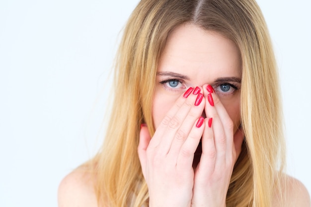 donna triste sconvolta che copre il viso con le mani sul muro bianco.