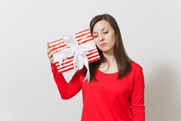 Donna turbata triste che tiene scatola attuale a strisce rossa con il nastro, arco isolato su fondo bianco. Per la pubblicità. San Valentino, Giornata internazionale della donna, Natale, compleanno, concetto di vacanza.