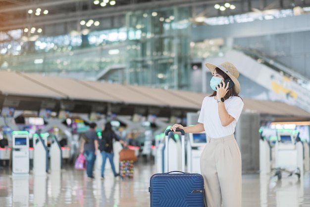 Donna turistica asiatica che indossa una maschera facciale e utilizza lo smartphone mobile nella protezione dell'aeroporto Infezione da malattia di coronavirus Tempo di viaggiare dopo il concetto di dose di richiamo del vaccino