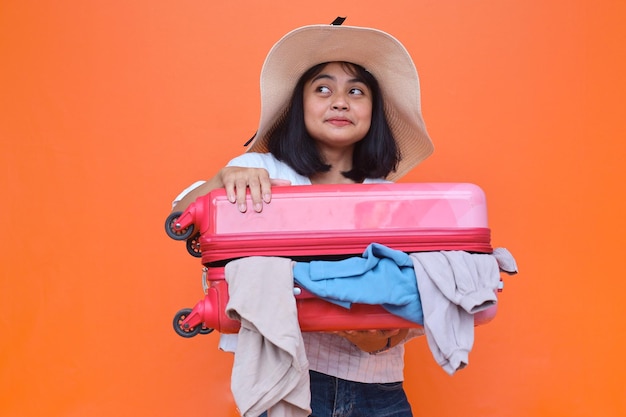 Donna turistica asiatica in cappello estivo che tiene la valigia aperta. Concetto di viaggio