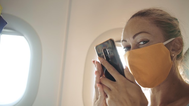 Donna turistica caucasica in viaggio su aereo aereo con maschera medica protettiva Ragazza che parla di coronovirus sul telefono cellulare smartphone Epidemia di virus sarscov2 covid19 2019ncov