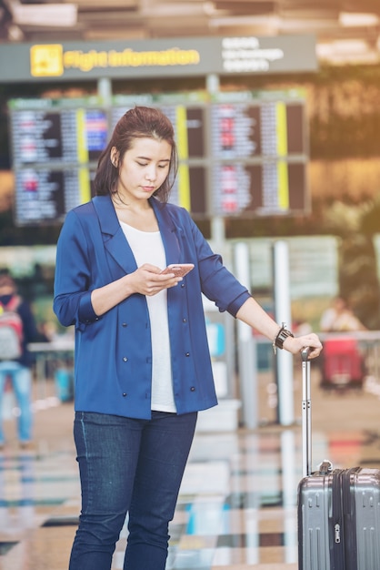 Donna turistica con bagagli in aeroporto. Felice giovane viaggiatore con il cellulare.