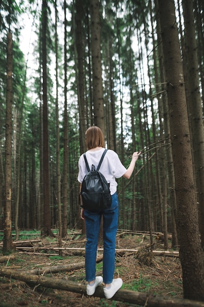 Donna turistica con uno zaino in piedi nella foresta di conifere toccando l'albero di pino