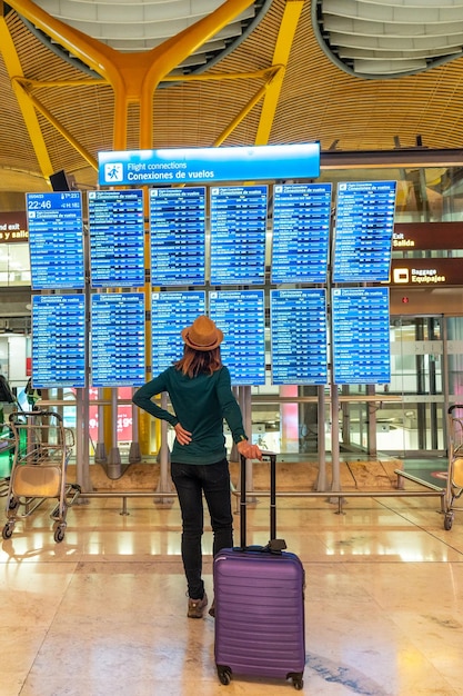 Donna turistica con valigia all'aeroporto che guarda le informazioni sugli schermi del terminal