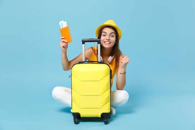 Donna turistica del viaggiatore in cappello giallo dell'abbigliamento casual di estate che tiene i bagagli dei biglietti sul blu