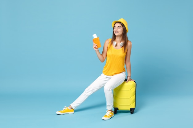 Donna turistica del viaggiatore in cappello giallo dell'abbigliamento casual di estate che tiene i bagagli dei biglietti sul blu