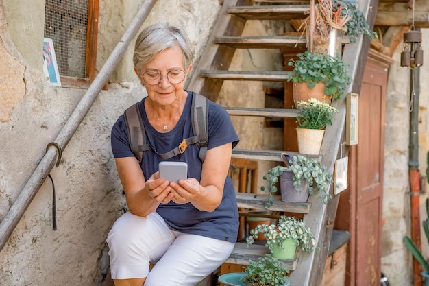 Donna turistica maggiore attraente che si siede su una scala di legno che digita sul telefono cellulare