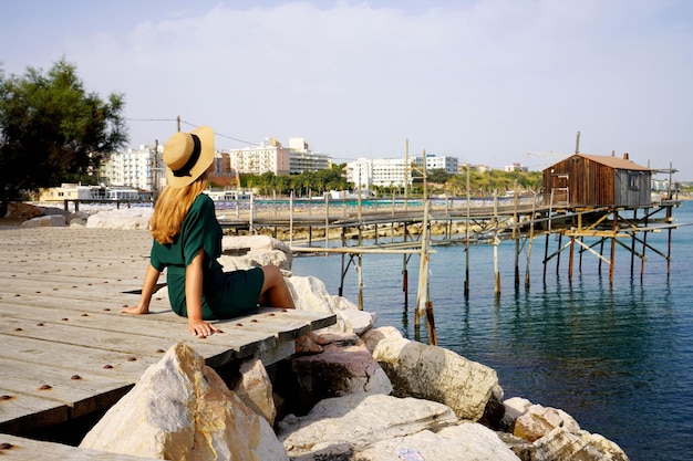 Donna turistica seduta sul lungomare rilassata con trabucco tradizionale macchina da pesca nel villaggio di Termoli Molise Italia