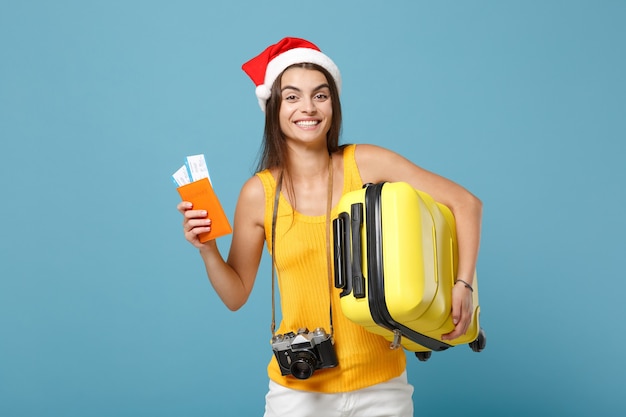 Donna turistica viaggiatrice con cappello da Babbo Natale, abiti casual gialli che tengono la macchina fotografica della borsa dei biglietti sul blu