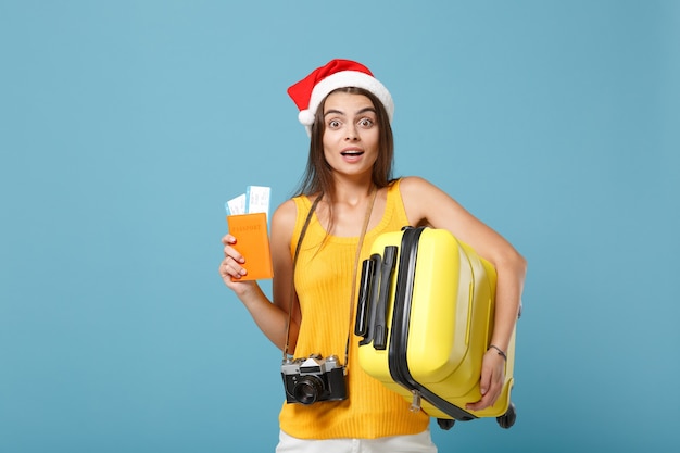 Donna turistica viaggiatrice con cappello da Babbo Natale, abiti casual gialli che tengono la macchina fotografica della borsa dei biglietti sul blu