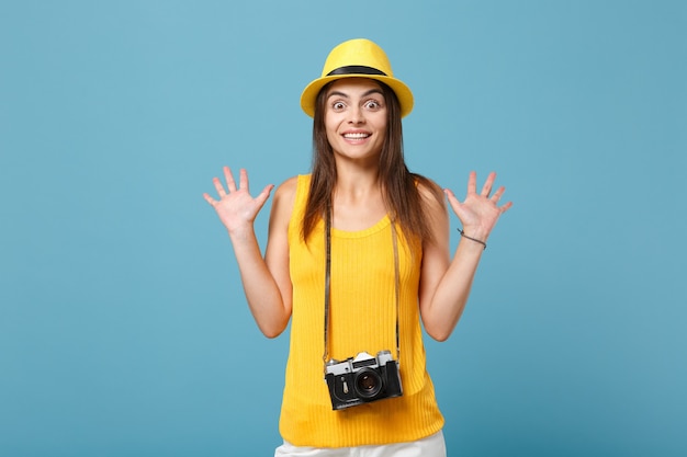 Donna turistica viaggiatrice in abiti casual estivi gialli, cappello con macchina fotografica isolata sulla parete blu. Passeggero femminile che viaggia all'estero per viaggiare nei fine settimana. Concetto di viaggio aereo.