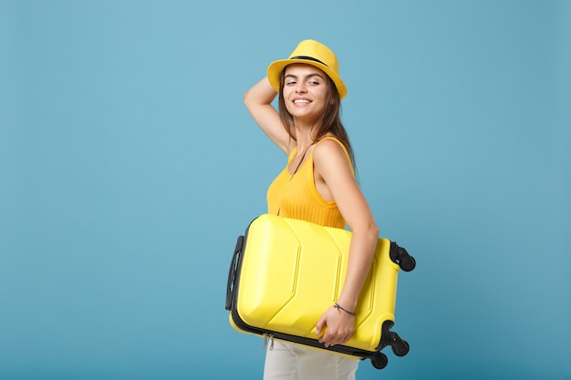 Donna turistica viaggiatrice in abiti casual gialli, cappello con macchina fotografica valigia su blu