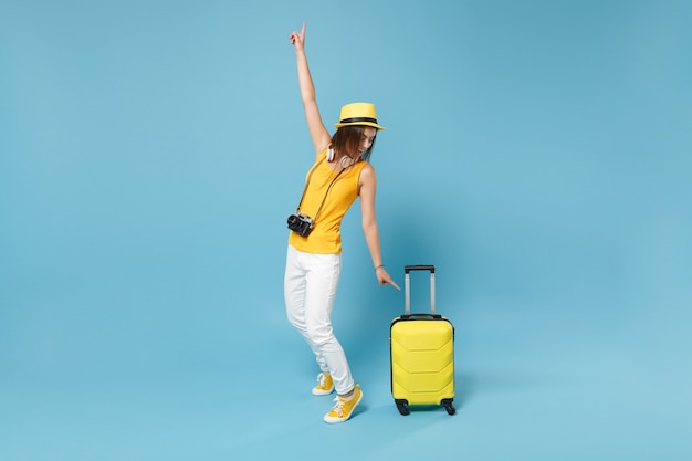 Donna turistica viaggiatrice in abiti casual gialli, cappello con macchina fotografica valigia su blu