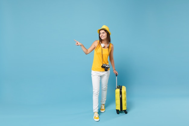 Donna turistica viaggiatrice in abiti casual gialli, cappello con macchina fotografica valigia su blu