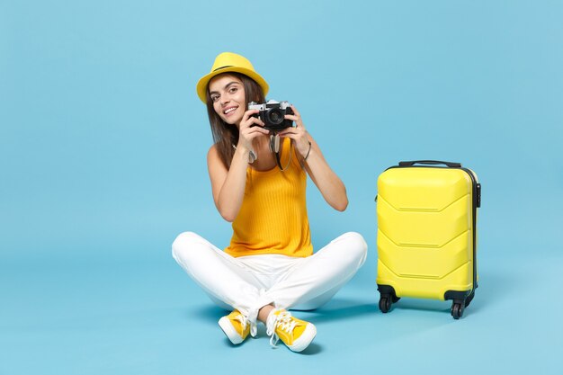 Donna turistica viaggiatrice in abiti casual gialli, cappello con macchina fotografica valigia su blu